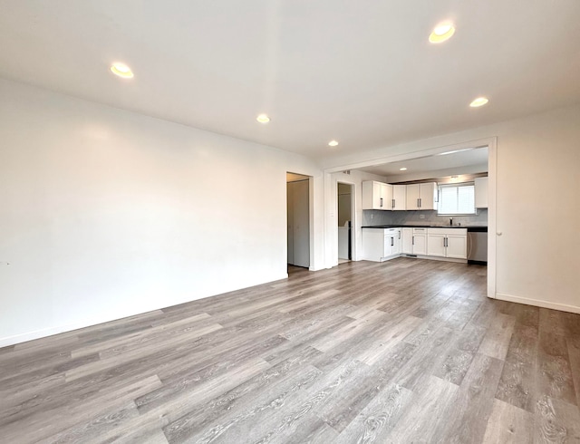 unfurnished living room with baseboards, light wood-type flooring, a sink, and recessed lighting