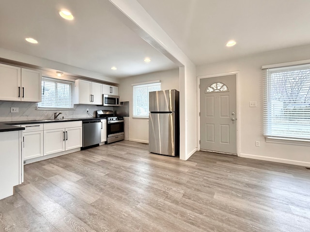 kitchen with stainless steel appliances, dark countertops, a wealth of natural light, and light wood finished floors