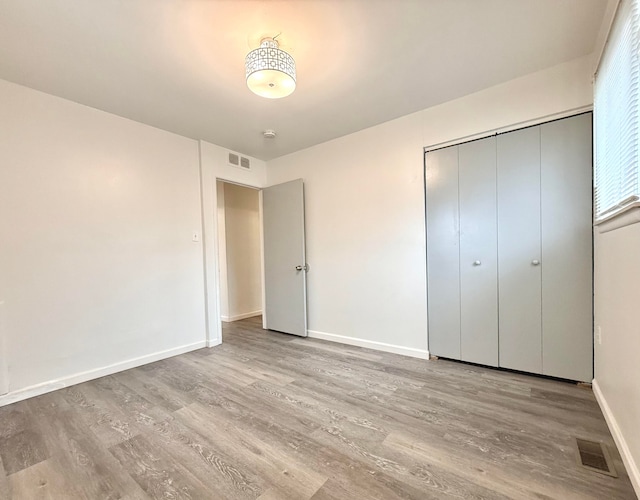 unfurnished bedroom featuring a closet, visible vents, baseboards, and wood finished floors