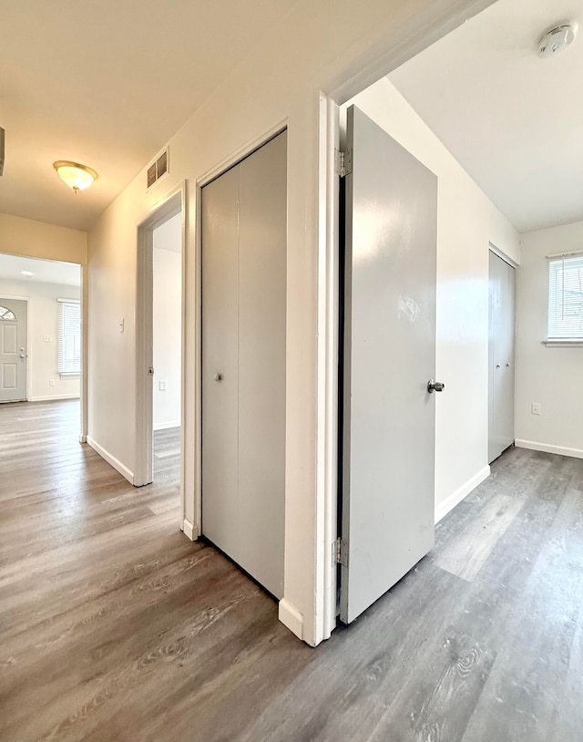 corridor with baseboards, visible vents, and wood finished floors