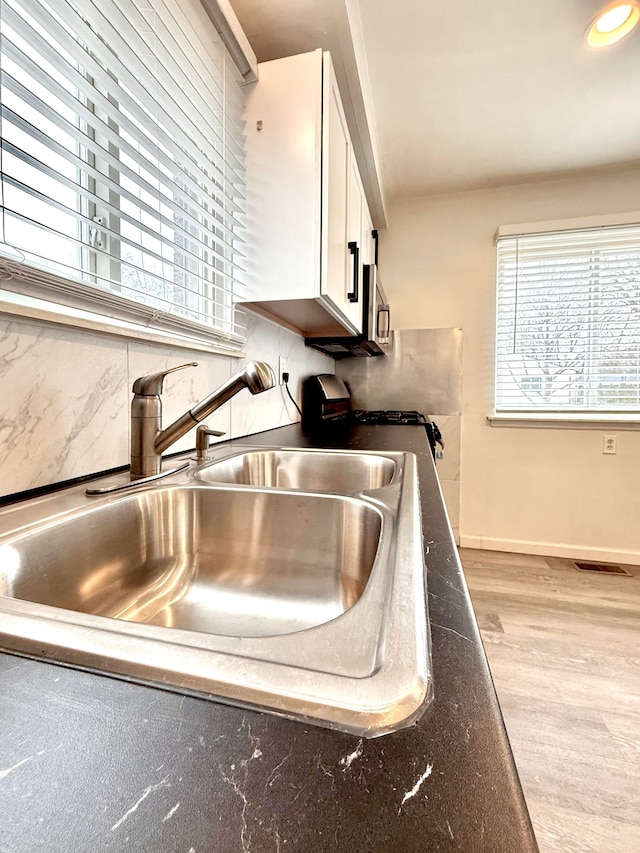 kitchen featuring a sink, visible vents, white cabinetry, light wood-style floors, and stainless steel microwave