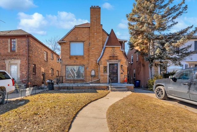 tudor home featuring brick siding, a chimney, and a front lawn