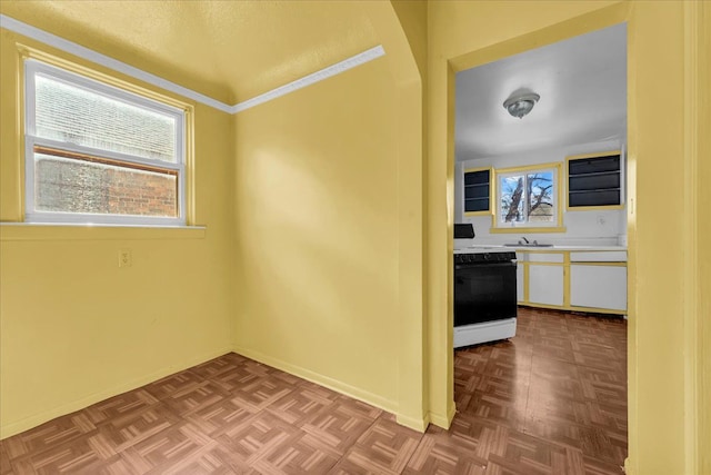 kitchen with gas range oven, light countertops, white cabinets, a sink, and baseboards