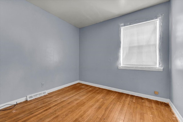 empty room with hardwood / wood-style floors, visible vents, and baseboards