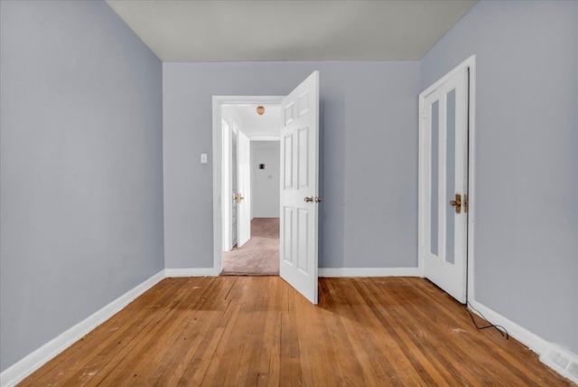 spare room featuring hardwood / wood-style floors, visible vents, and baseboards