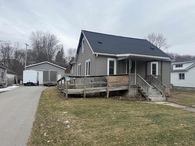 view of front of property featuring a garage, roof with shingles, a front yard, and an outbuilding