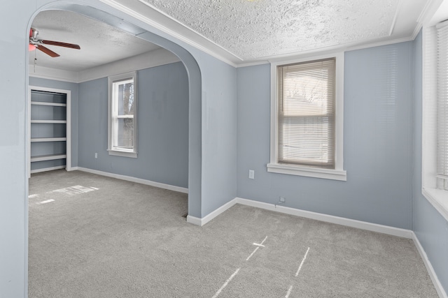 carpeted spare room featuring arched walkways, a textured ceiling, and baseboards