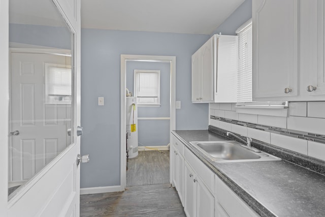 kitchen with dark countertops, backsplash, dark wood finished floors, white cabinets, and a sink