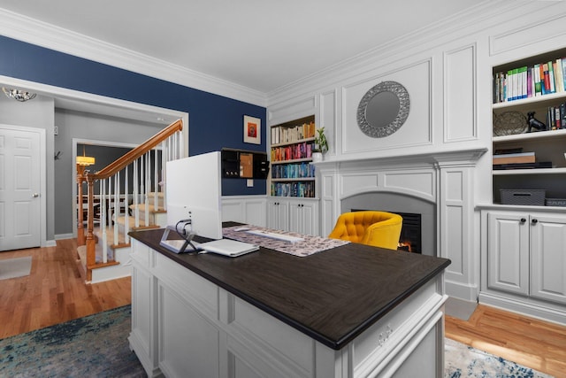 office area featuring built in shelves, light wood-type flooring, crown molding, and a lit fireplace