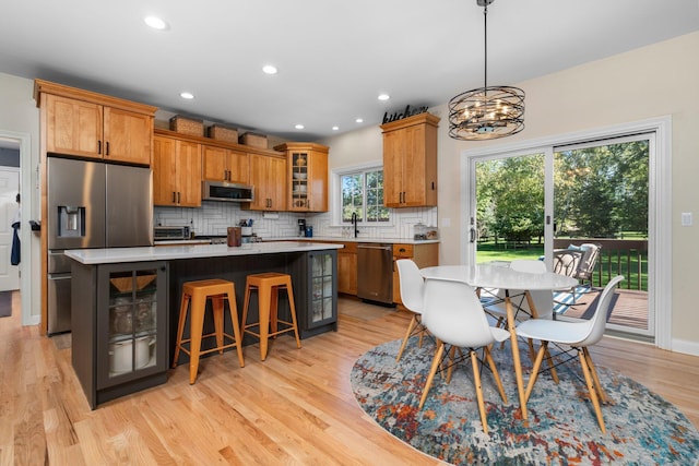 kitchen with stainless steel appliances, a kitchen island, decorative backsplash, brown cabinets, and light wood finished floors