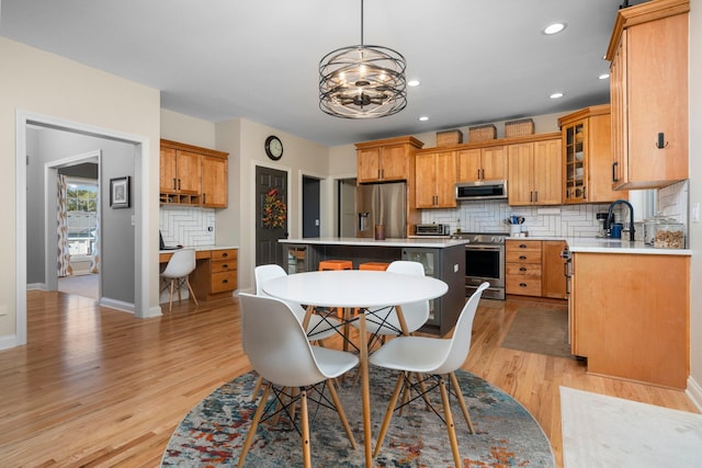 kitchen with light wood-style flooring, appliances with stainless steel finishes, a center island, light countertops, and backsplash