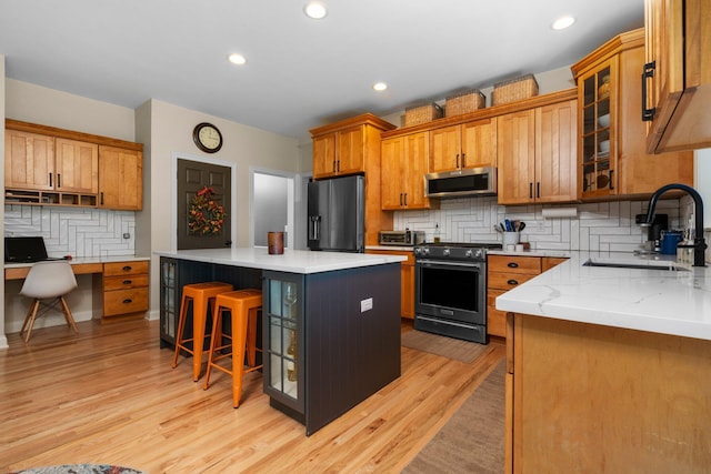 kitchen with light wood-style flooring, a sink, appliances with stainless steel finishes, a center island, and built in desk