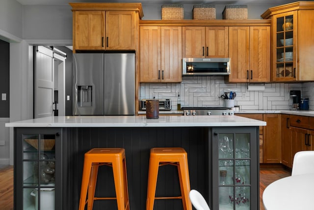 kitchen featuring brown cabinetry, a barn door, appliances with stainless steel finishes, and decorative backsplash