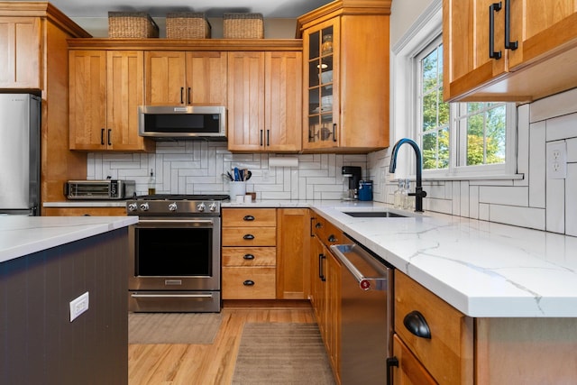 kitchen featuring appliances with stainless steel finishes, a sink, decorative backsplash, and light stone counters