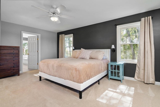 carpeted bedroom featuring ensuite bathroom, multiple windows, a ceiling fan, and baseboards