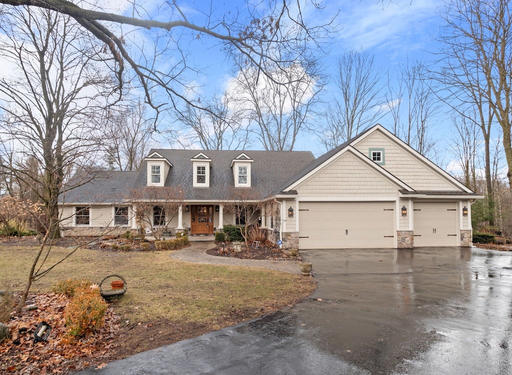 view of front of home featuring driveway, a garage, stone siding, a porch, and a front lawn