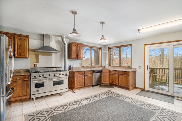 kitchen featuring decorative light fixtures, light tile patterned floors, appliances with stainless steel finishes, brown cabinetry, and wall chimney exhaust hood