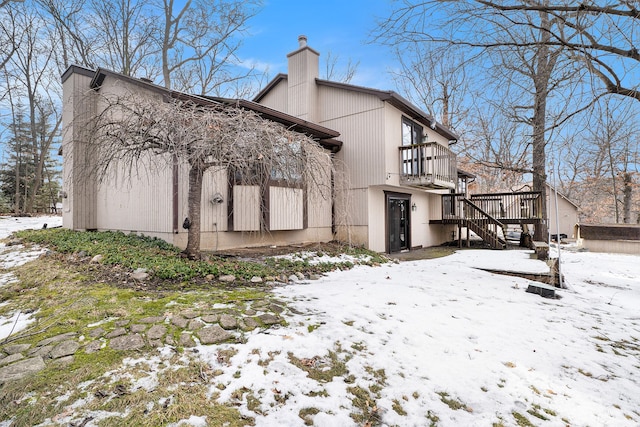 snow covered house featuring a chimney and stairway