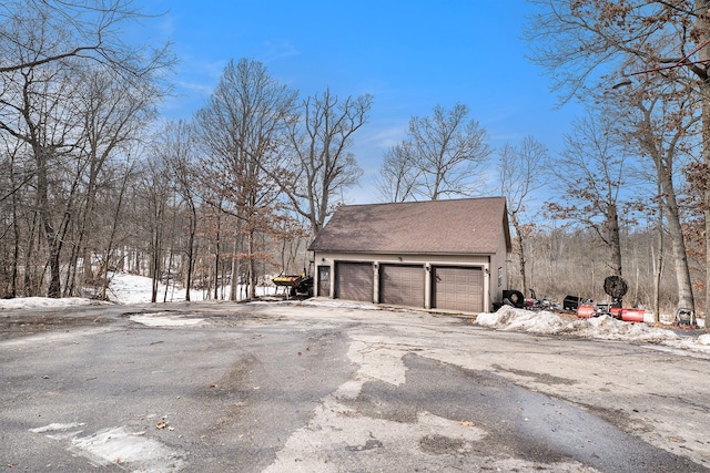 snow covered property featuring a shingled roof, an outbuilding, and a detached garage