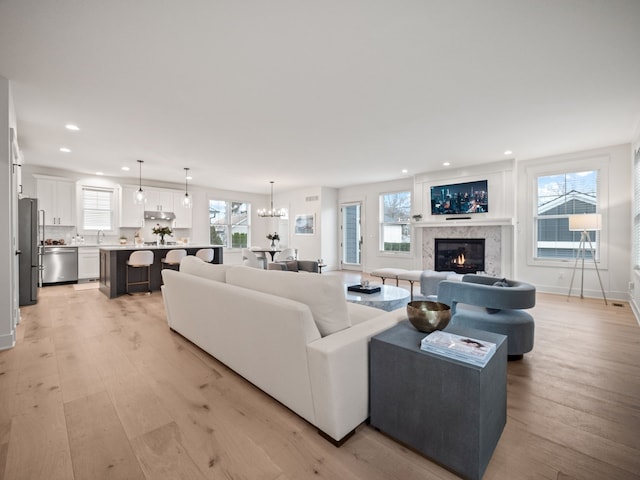 living area featuring baseboards, light wood-type flooring, recessed lighting, a fireplace, and an inviting chandelier