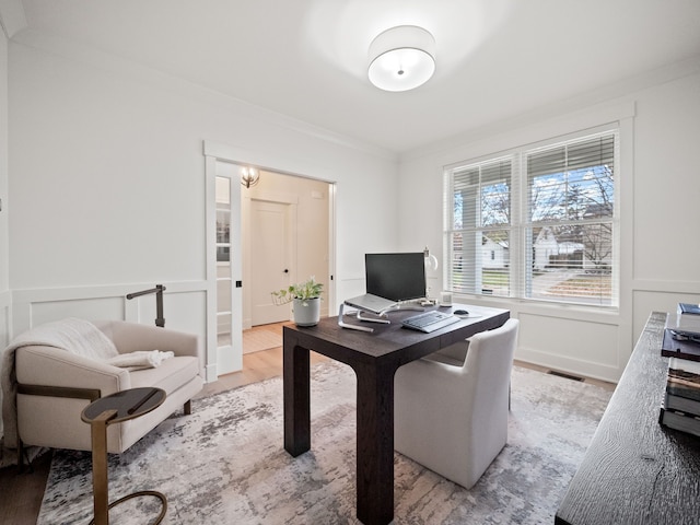 office space featuring visible vents, light wood finished floors, wainscoting, crown molding, and a decorative wall