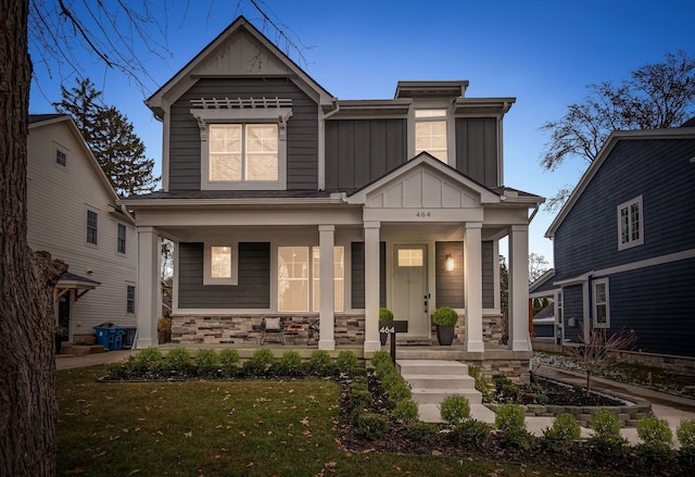 craftsman inspired home with a porch, stone siding, board and batten siding, and a front yard