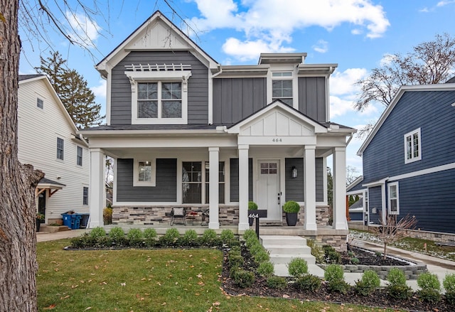 view of front of house featuring stone siding, covered porch, board and batten siding, and a front lawn