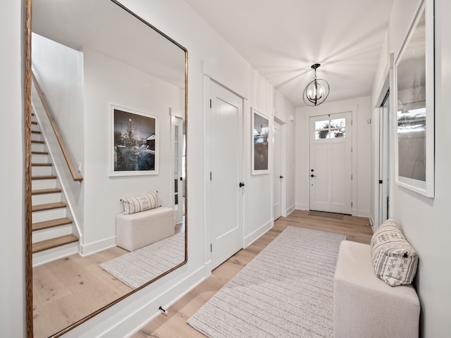 foyer featuring light wood-style floors, baseboards, a notable chandelier, and stairs