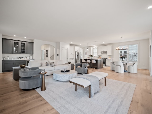 living area with recessed lighting, arched walkways, light wood-style floors, baseboards, and a chandelier