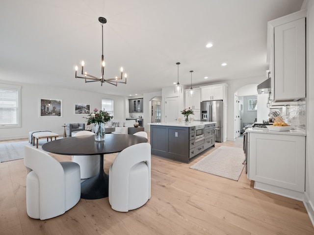 dining room featuring arched walkways, a healthy amount of sunlight, light wood-type flooring, and an inviting chandelier