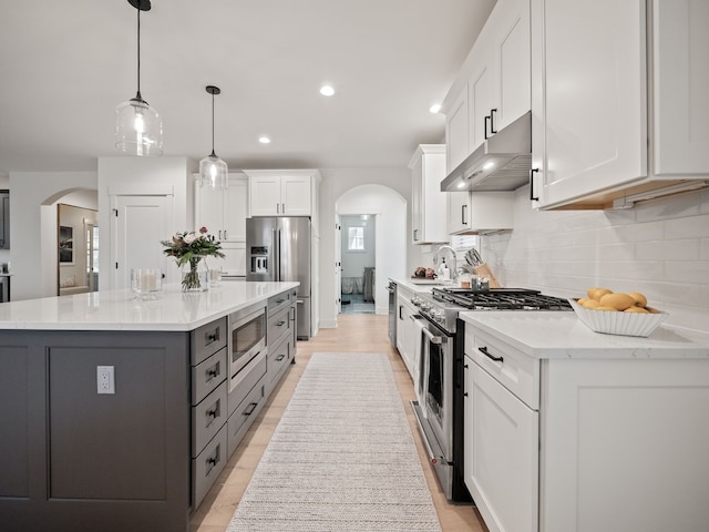 kitchen with under cabinet range hood, tasteful backsplash, stainless steel appliances, arched walkways, and white cabinets