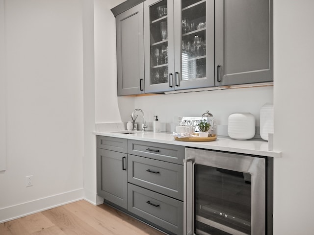 bar with a sink, light wood-type flooring, wine cooler, and baseboards