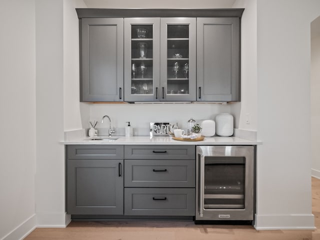 bar with wine cooler, light wood-style flooring, baseboards, and a sink