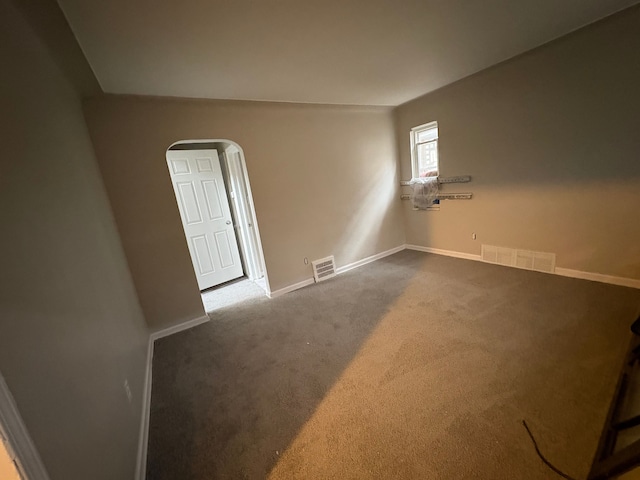 unfurnished room with baseboards, visible vents, arched walkways, and dark colored carpet