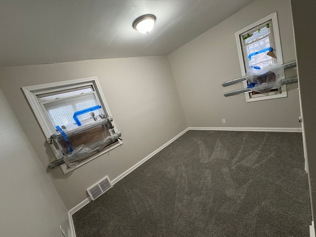 empty room with dark carpet, visible vents, and baseboards