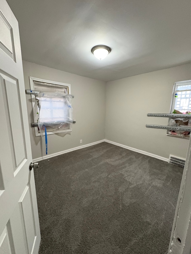 empty room featuring dark carpet, visible vents, and baseboards