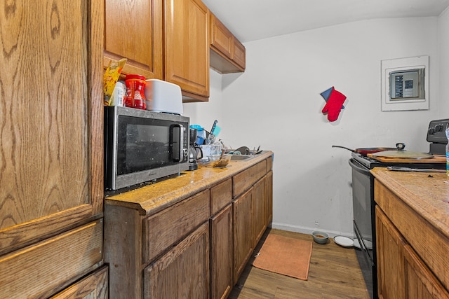 kitchen featuring brown cabinetry, wood finished floors, baseboards, and black electric range