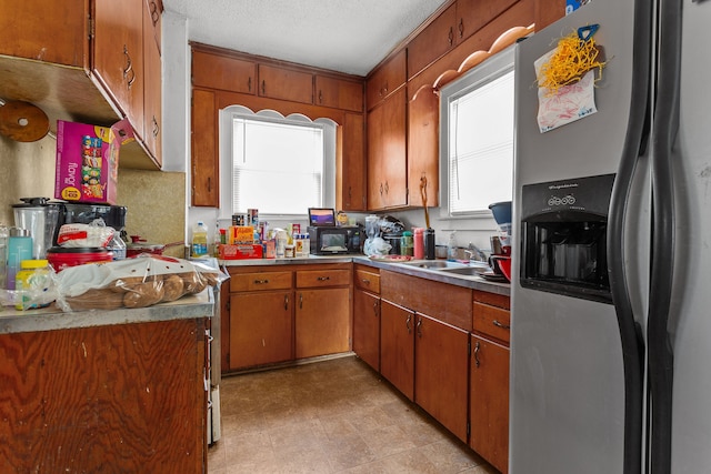 kitchen featuring a sink, a textured ceiling, stainless steel refrigerator with ice dispenser, and brown cabinets