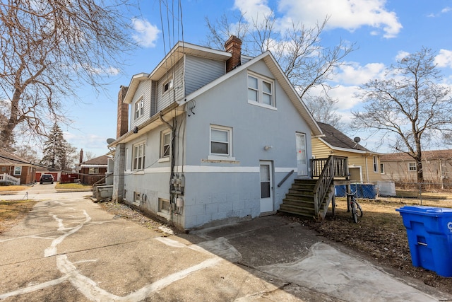 view of property exterior featuring concrete driveway, fence, and a chimney