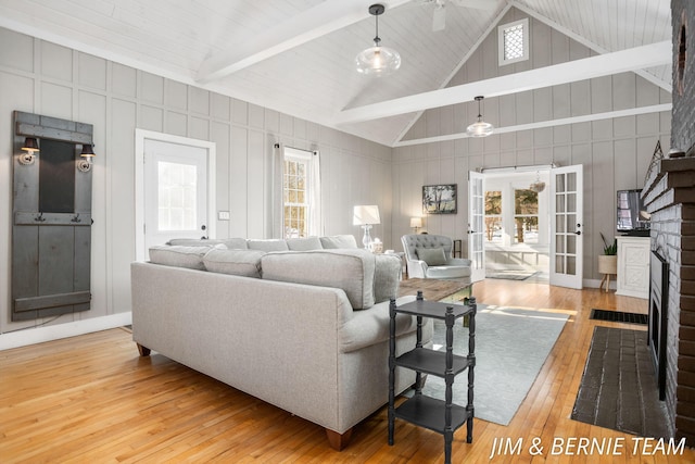 living area featuring wood-type flooring, a brick fireplace, beamed ceiling, high vaulted ceiling, and french doors
