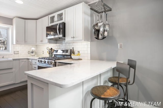 kitchen with light stone countertops, appliances with stainless steel finishes, a breakfast bar area, a peninsula, and decorative backsplash