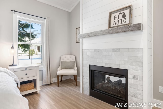 bedroom featuring a glass covered fireplace, baseboards, and light wood finished floors
