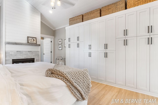 bedroom with ceiling fan, a large fireplace, light wood-type flooring, vaulted ceiling, and ornamental molding