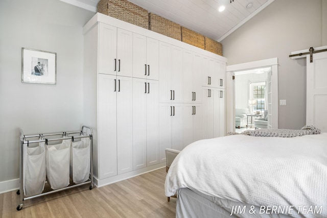 bedroom with a barn door, light wood finished floors, and high vaulted ceiling