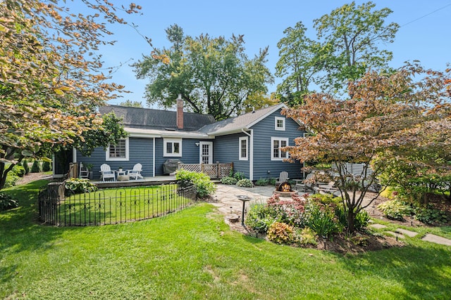 rear view of property featuring a lawn, a chimney, a fire pit, and a deck