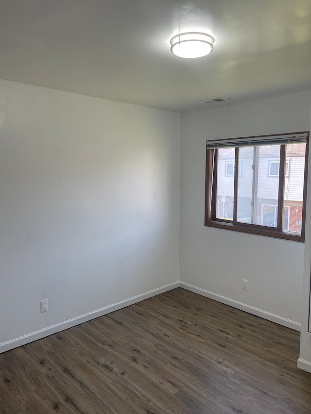 unfurnished room featuring dark wood-style floors, visible vents, and baseboards