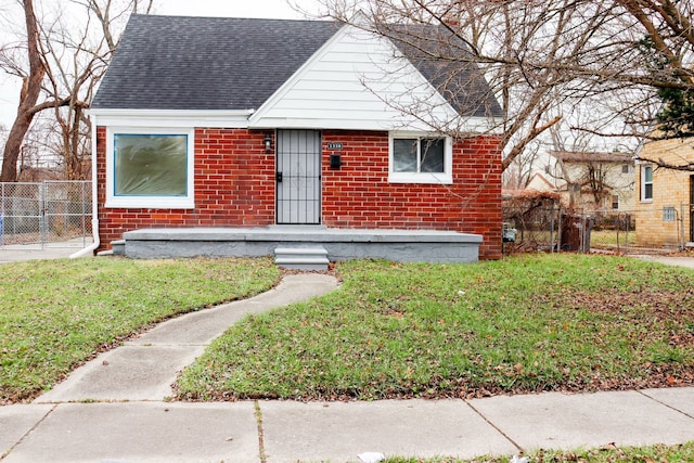 bungalow-style house featuring a shingled roof, a gate, fence, a front lawn, and brick siding