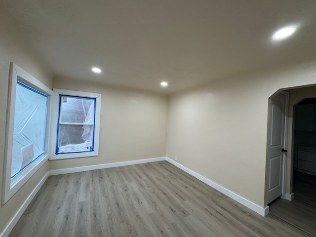 unfurnished room with recessed lighting, arched walkways, baseboards, and wood finished floors