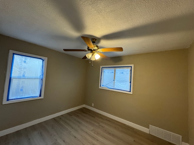 spare room featuring visible vents, ceiling fan, a textured ceiling, wood finished floors, and baseboards