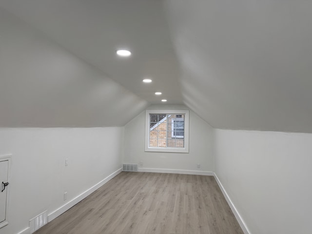 additional living space featuring light wood-type flooring, baseboards, visible vents, and vaulted ceiling